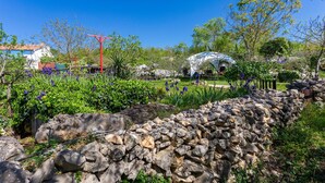 Un jardin avec un mur en pierre, une structure métallique rouge et une structure blanche en forme de tente.