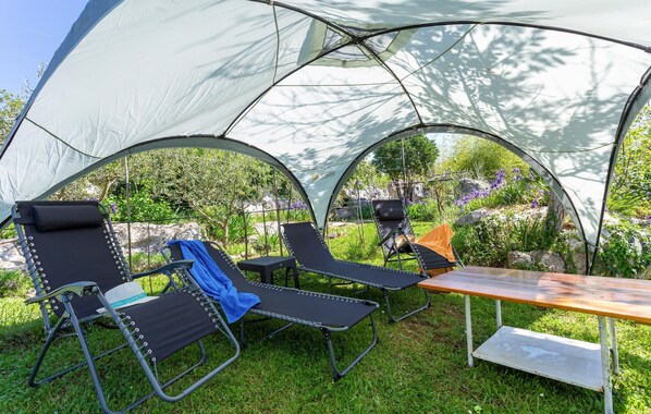 A tent with two reclining chairs and a table, set in a grassy area with rocks and plants.