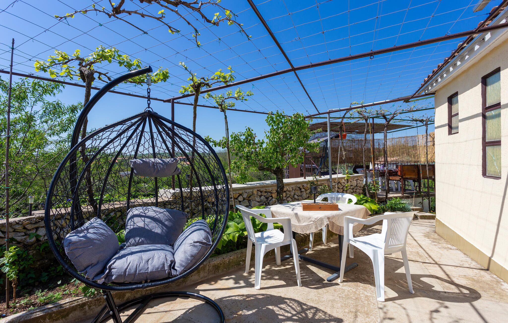 Une terrasse avec un fauteuil suspendu, des chaises en plastique blanches et une table.