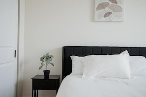 A neatly made bed with white linens, a black headboard, and a small bedside table with a potted plant. - New build modern home 3BR with Hot Tub & ping pong (Delaware)
