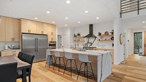 A modern kitchen with a central island, wooden cabinets, and a stainless steel refrigerator. - Sandy River Group Getaway (Mount Hood Village)