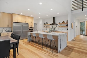 A modern kitchen with a central island, wooden cabinets, and a stainless steel refrigerator. - Sandy River Group Getaway (Mount Hood Village)