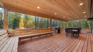 A covered outdoor area with a wooden deck, a bench, a grill, and a table with chairs. - Sandy River Group Getaway (Mount Hood Village)