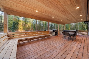 A covered outdoor area with a wooden deck, a bench, a grill, and a table with chairs. - Sandy River Group Getaway (Mount Hood Village)