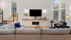 A modern living room with a large flat-screen TV, a fireplace, and a staircase. - Sandy River Group Getaway (Mount Hood Village)