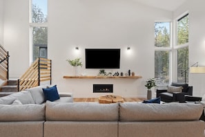 A modern living room with a large flat-screen TV, a fireplace, and a staircase. - Sandy River Group Getaway (Mount Hood Village)