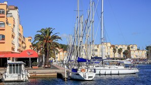 Un porto turistico con diverse barche a vela ormeggiate, una palma e edifici con balconi.
