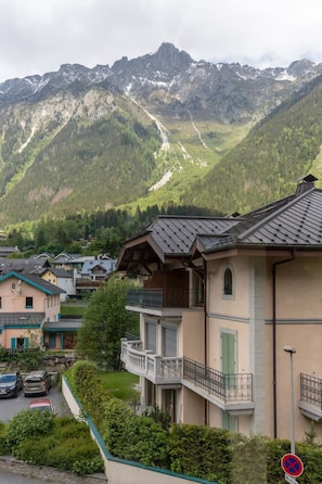 En boligbygning med balkon, omgivet af frodig vegetation og bjerge i baggrunden.