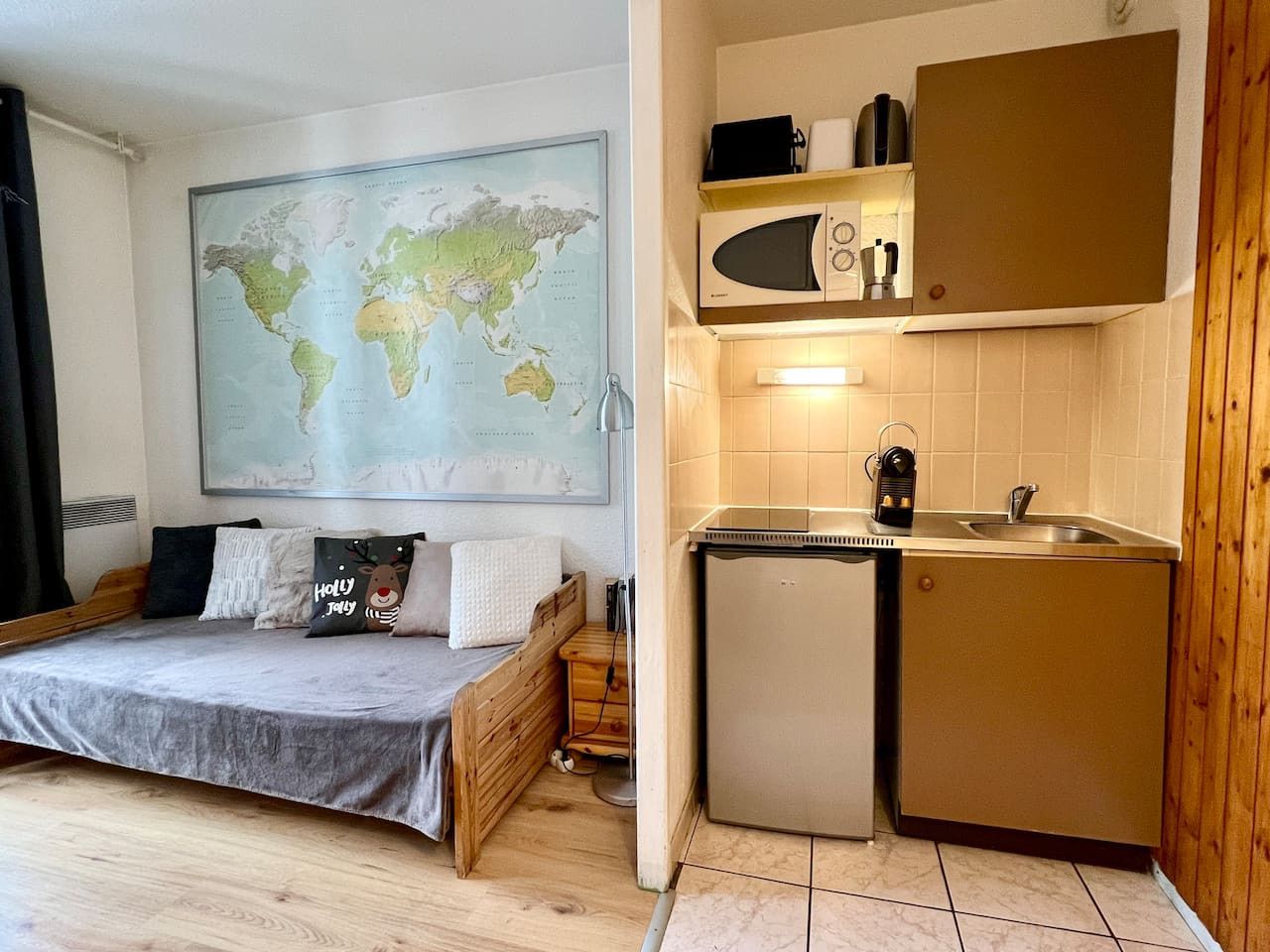Quarto compacto com cama, pequeno espaço de cozinha e um mapa-múndi na parede.