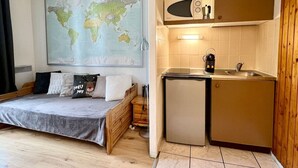 Ein kleines Zimmer mit einem Bett, einer kompakten Küchenzeile und einer Weltkarte an der Wand.