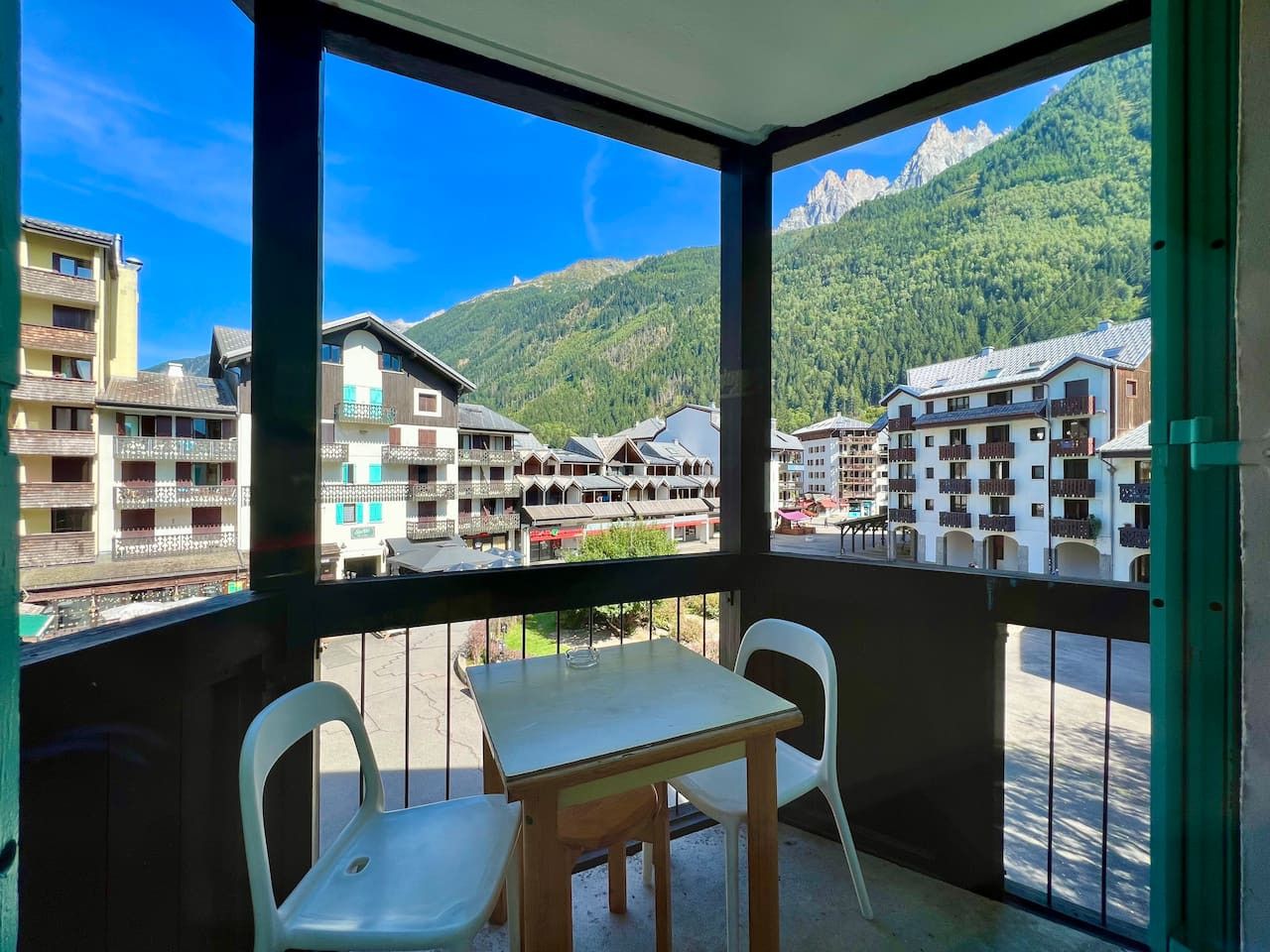 Varanda com mesa e cadeiras, vista para montanhas e edifícios.