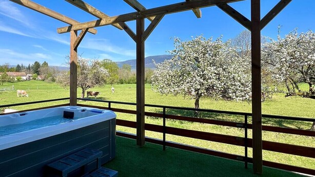 Ett bubbelbad under en träpergola med utsikt över en grön äng och blommande träd.