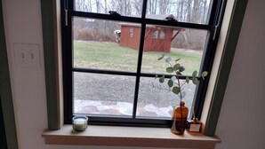 Janela com vista para um edifício vermelho, uma vela e um vaso com uma planta.