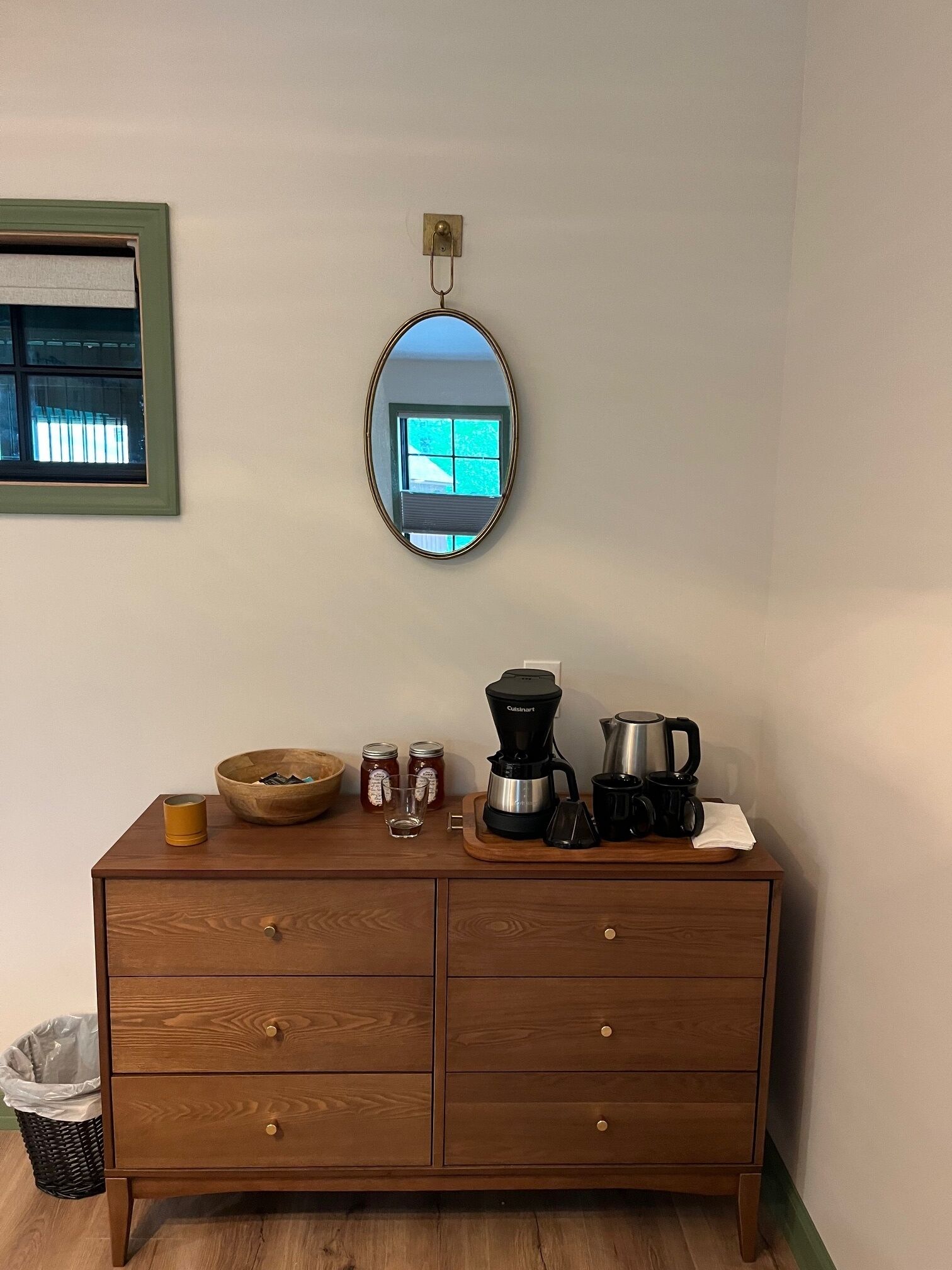 A wooden dresser with a mirror, a coffee maker, a bowl, jars, and a cup.