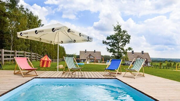 A swimming pool with four lounge chairs and a large umbrella.