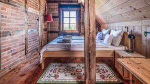 A cozy attic bedroom with exposed wooden beams, a brick wall, and a large window.