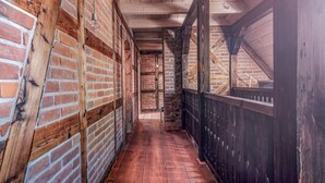 A narrow hallway with wooden floors and brick walls, featuring exposed wooden beams and a stone wall section.