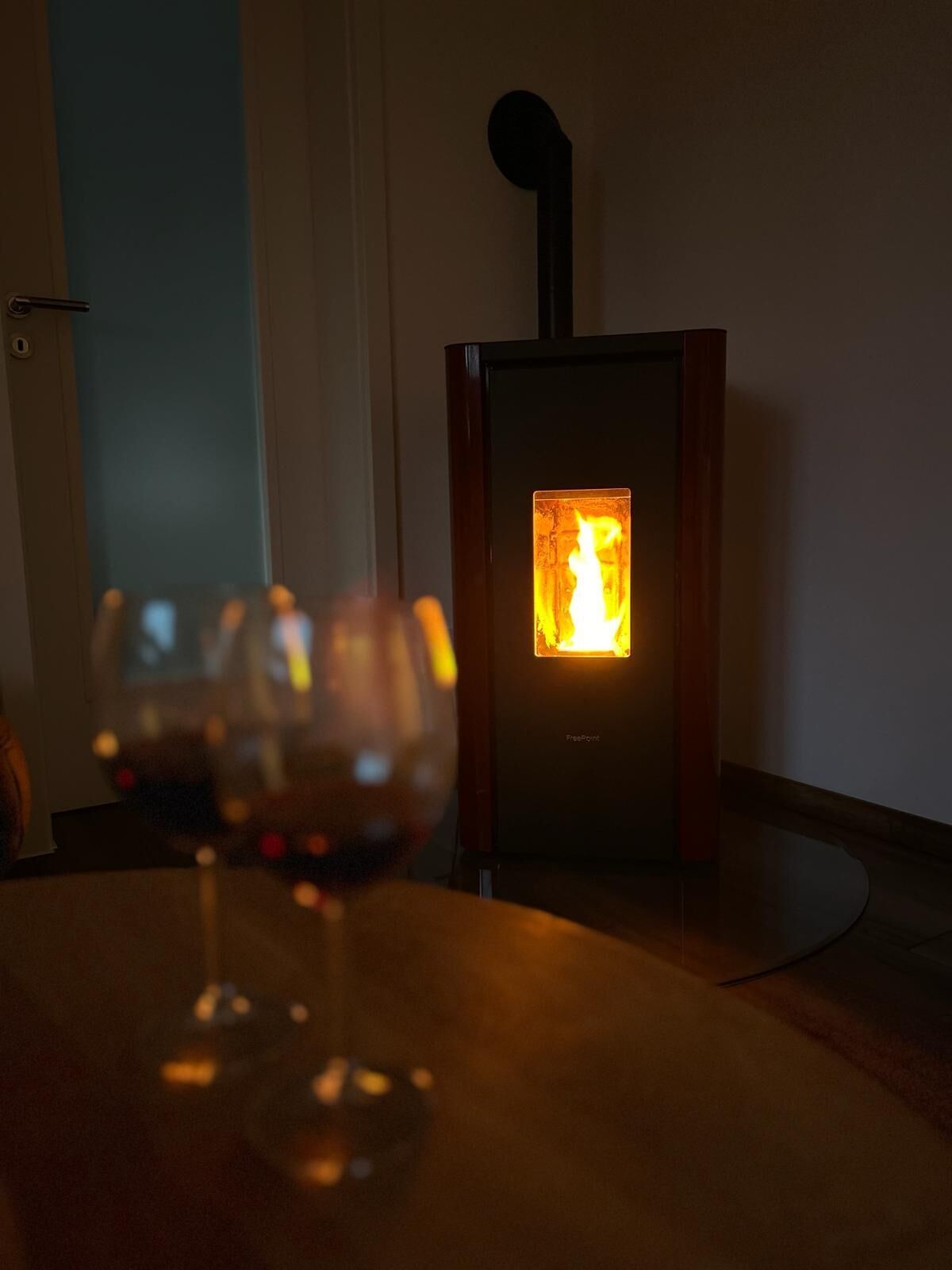 Un verre de vin rouge sur une table, avec un poêle à bois en arrière-plan.