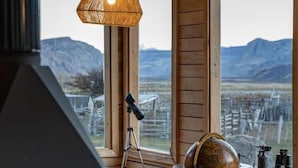 A cozy cabin interior with a large window offering a mountain view, a fireplace, and rustic furnishings. - Estancia Bonanza Patagonian Lodge Experience (El Chalten)