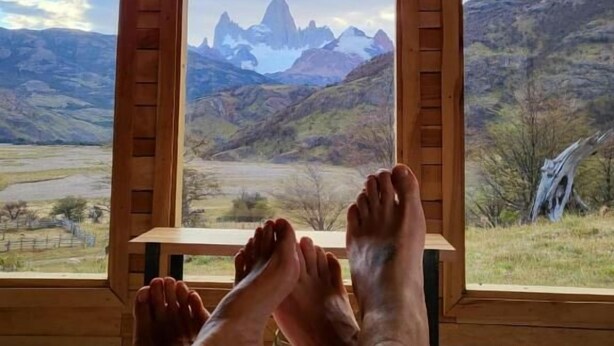 A room with a wooden ceiling and a large window with wooden shutters, offering a view of a mountainous landscape. - Estancia Bonanza Patagonian Lodge Experience (El Chalten)