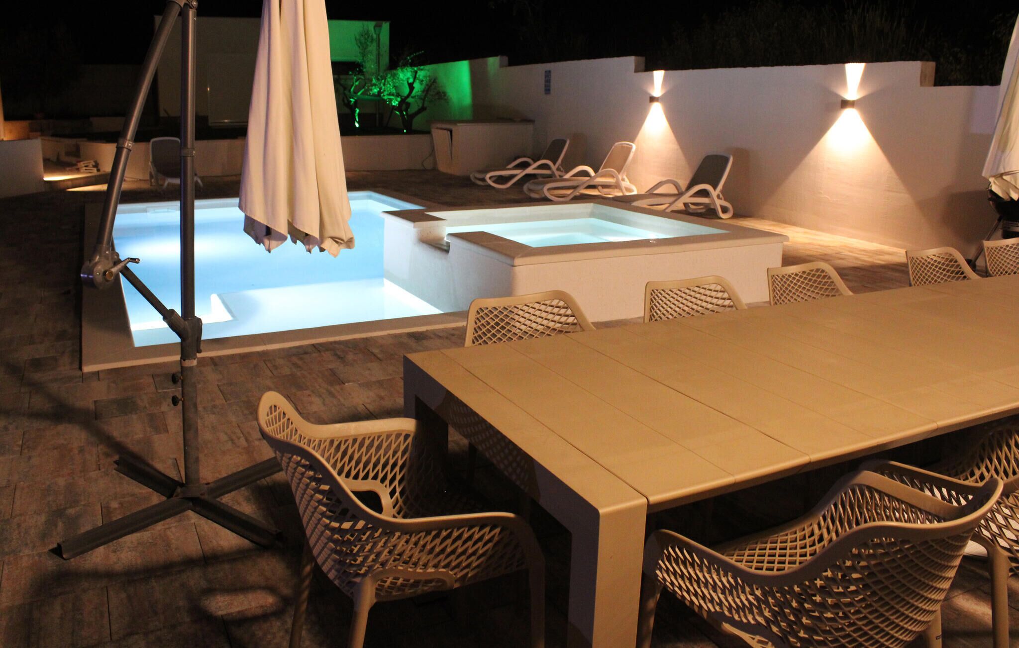 An outdoor pool area with lounge chairs and a table, surrounded by wicker chairs.