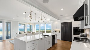 Una cocina moderna con una isla grande, muebles blancos y vistas al océano.