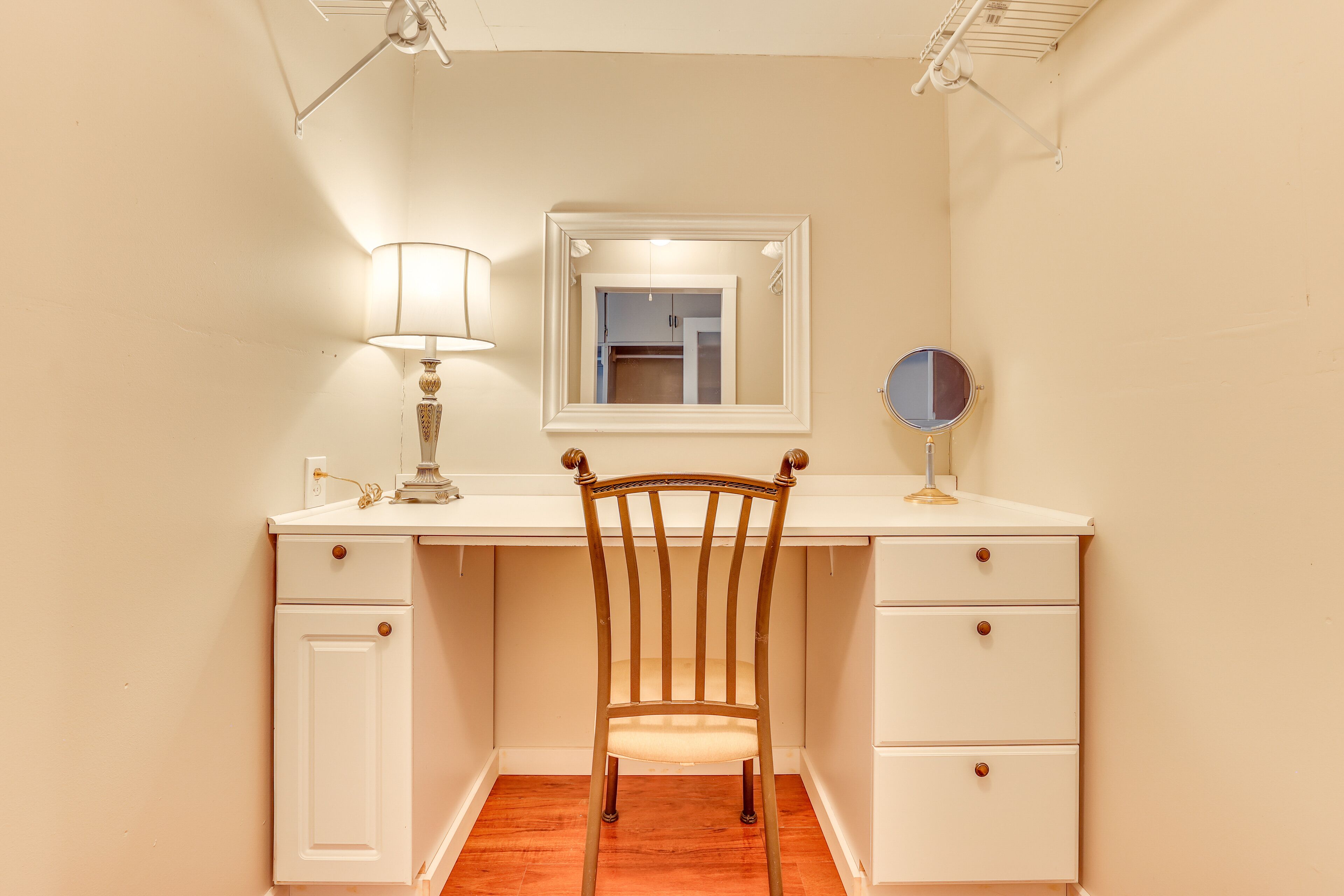 A compact bedroom with a wooden chair, a desk with drawers, a mirror, and a lamp.