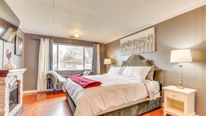 Une chambre à coucher comprenant un lit, une table de chevet, une chaise, une cheminée et une fenêtre avec des rideaux.