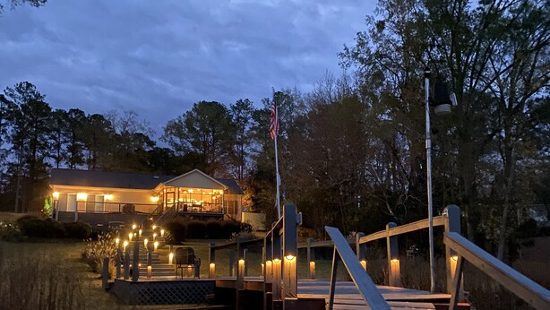 Un muelle de madera que conduce a una casa con porche e iluminación.