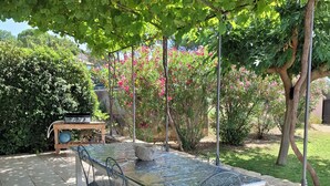 An outdoor patio with a glass-top table and metal chairs, surrounded by greenery and a stone wall.
