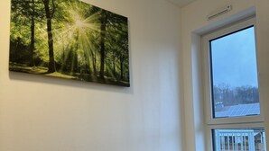 Une chambre à coucher avec un lit, une grande fenêtre donnant sur un paysage enneigé et un tableau représentant une forêt accroché au mur.