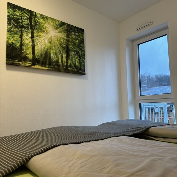 A bedroom with a bed, a large window with a view of a snowy landscape, and a forest painting on the wall.