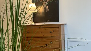 Une commode en bois avec des tiroirs, une lampe et un tableau représentant un cerf accroché au mur.
