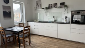 Une cuisine moderne avec des armoires blanches, un comptoir noir et un four encastré. Une fenêtre laisse entrer la lumière naturelle et offre une vue sur l’extérieur.