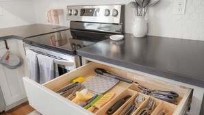 Une cuisine équipée d’un four en acier inoxydable, d’une machine à café et d’un organiseur de tiroir contenant des ustensiles.