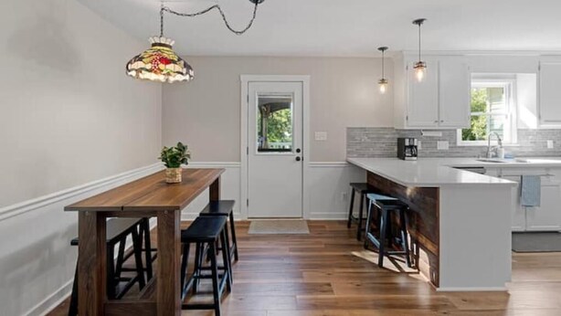 Une cuisine moderne avec une table à manger en bois, des tabourets de bar et des luminaires suspendus.