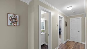 Un couloir avec un plancher en bois, des portes blanches et un tableau encadré accroché au mur.