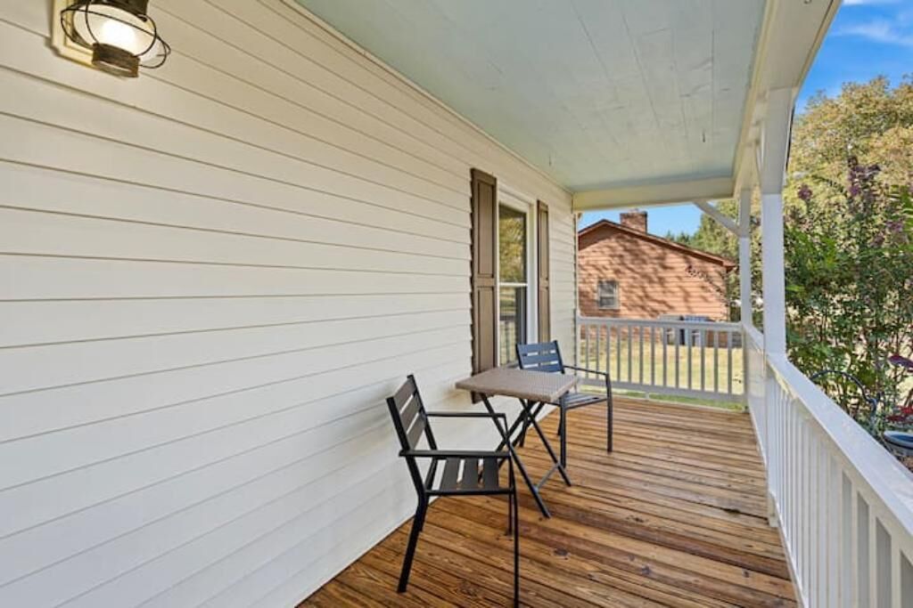 A covered porch with a wooden floor, white siding, and two chairs.
