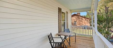 A covered porch with a wooden floor, white siding, and two chairs.