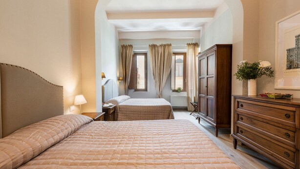 A hotel room with two beds, a wooden dresser, a nightstand, and a window with curtains. - Apartments Florence - Ariento Giuditta 2 bdr (Firenze)