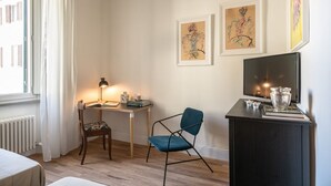 Une pièce comprenant un bureau, une chaise, des œuvres d’art accrochées au mur, un téléviseur et un radiateur.