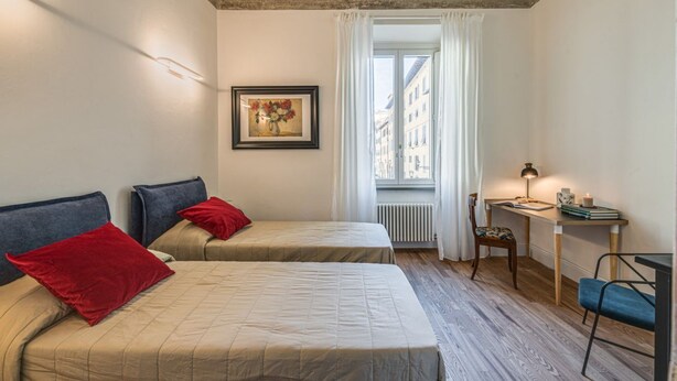 Une chambre avec deux lits, un bureau, une chaise, un radiateur et une fenêtre avec des rideaux.