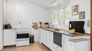 A modern kitchen with white cabinets, a wooden countertop, and a black range hood. There are windows with white frames and a poster on the wall. - Nice home in Jægerspris with kitchen (Jægerspris)