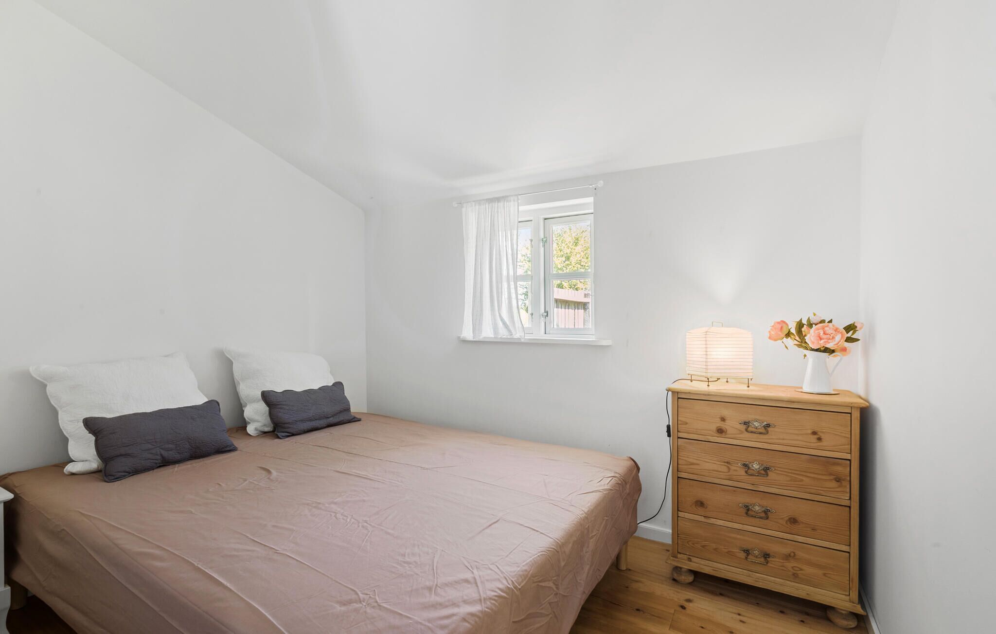 Un dormitorio con cama, cómoda, ventana y lámpara.