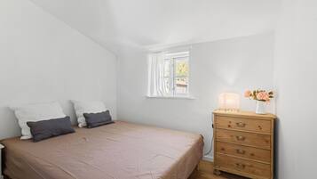Un dormitorio con cama, cómoda, ventana y lámpara.