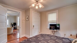 Un dormitorio con una cama grande, un ventilador de techo, un televisor sobre un mueble y una puerta que da a otra habitación.