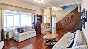 A spacious living room with hardwood flooring, a large window, a ceiling fan, a staircase, and a bookshelf. - Large Three Bedroom Retreat Family Friendly Cottage (MacTier)