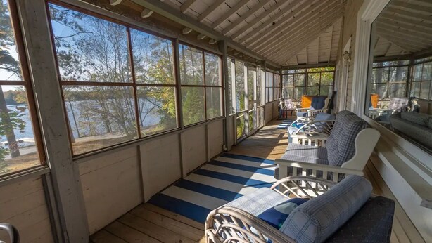 A covered porch with wooden flooring, striped rugs, and wicker furniture. - Large Three Bedroom Retreat Family Friendly Cottage (MacTier)