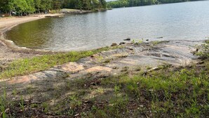 A natural lakeside setting with a rocky shoreline, dense forest in the background, and a clear sky. - Large Three Bedroom Retreat Family Friendly Cottage (MacTier)