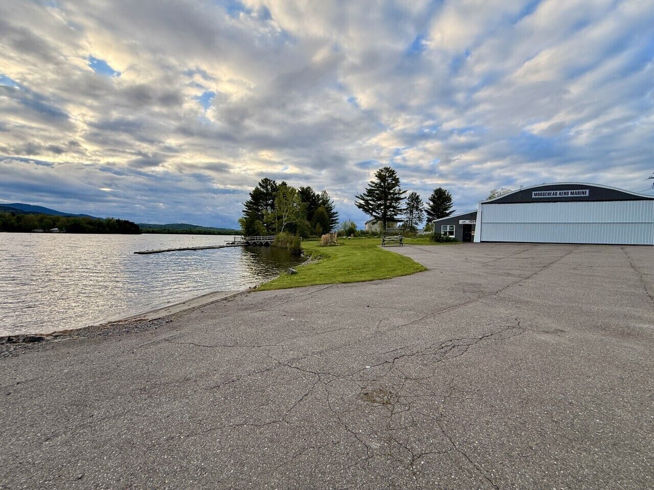 Un grand bâtiment sur lequel on peut lire l’inscription « MOOSEHEAD AERO MARINE », situé près d’une étendue d’eau, avec une zone herbeuse et des arbres.